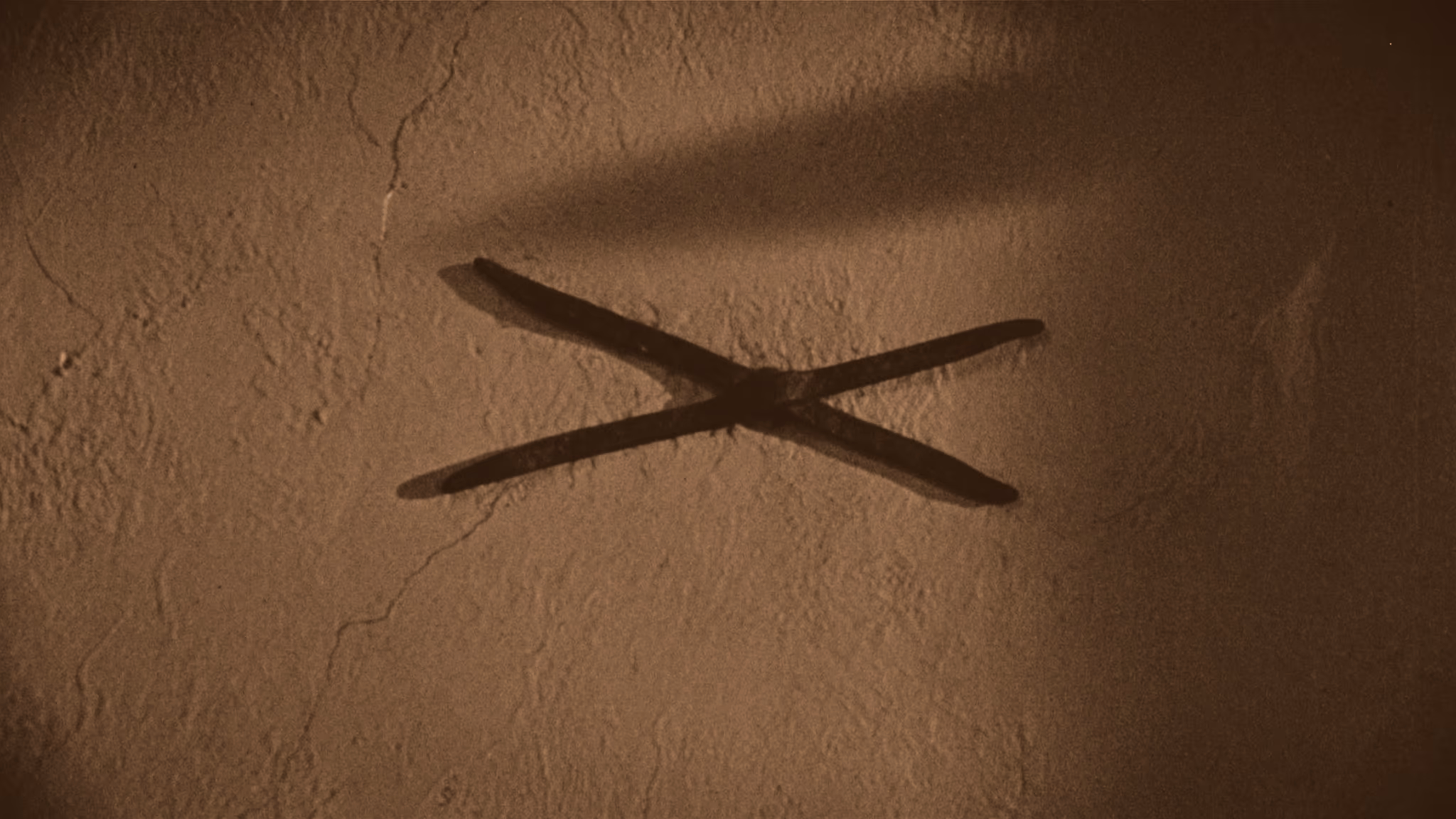 A wrought-iron X wall anchor set into weathered whitewashed plaster