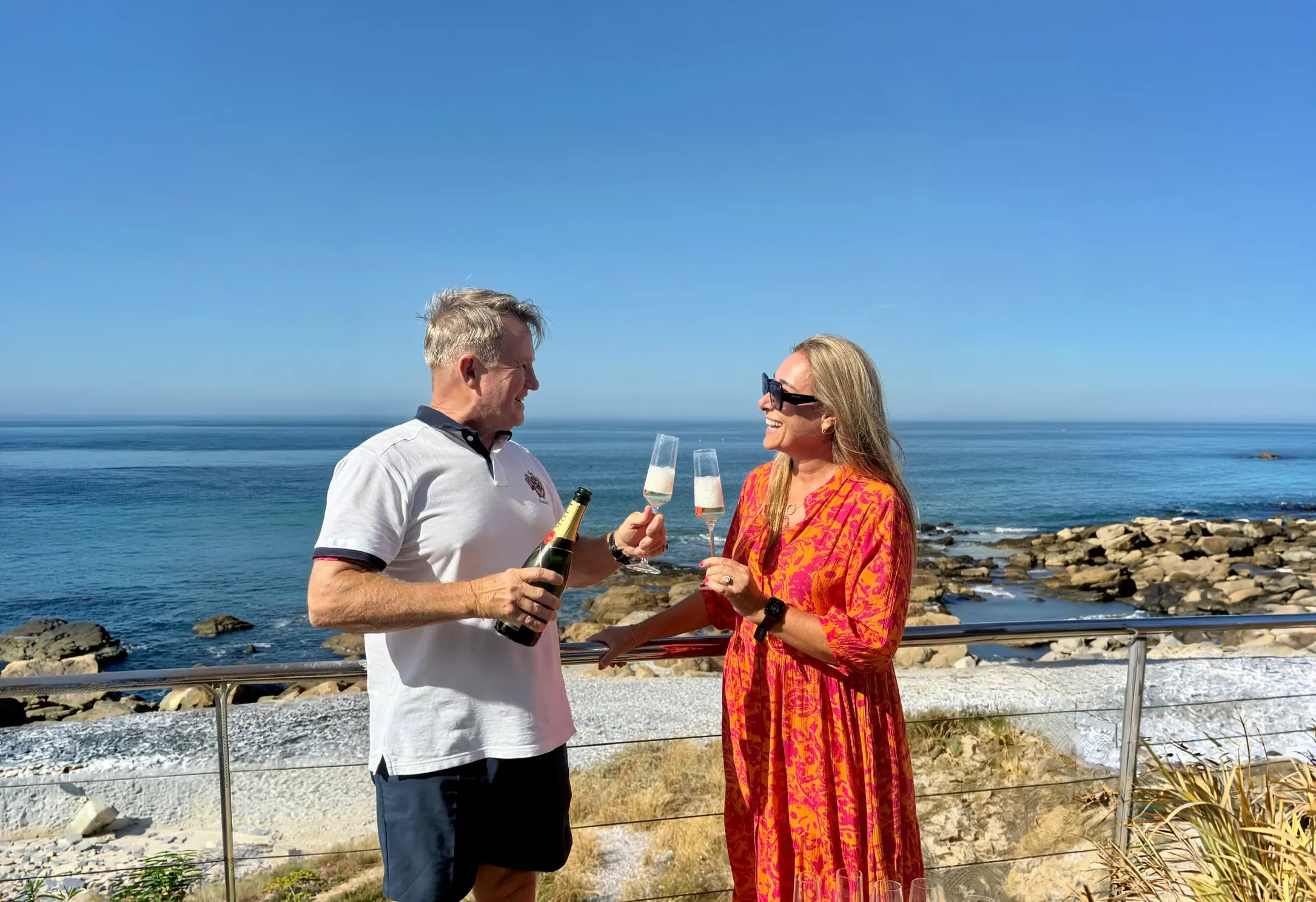 Timothy and Kathrin raising a glass above the sea