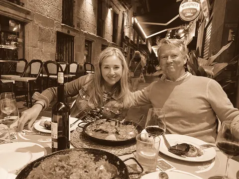 A pan of paella between them at a pavement table