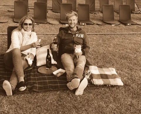 A picnic rug on cut grass, a bottle open between them